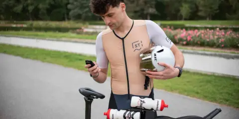 Kolarz sprawdza na telefonie, jaka kadencja na rowerze jest optymalna. Trzyma kask, gotowy do startu.