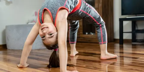 Uśmiechnięta dziewczynka w sportowym stroju wykonuje mostek. To świetna gimnastyka dla dzieci, rozwijająca gibkość i siłę.