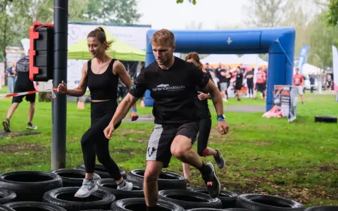 Zawodnicy pokonują tor przeszkód z opon. Kobieta i mężczyzna biegną, a za nimi inni uczestnicy. To prawdziwa survival race!