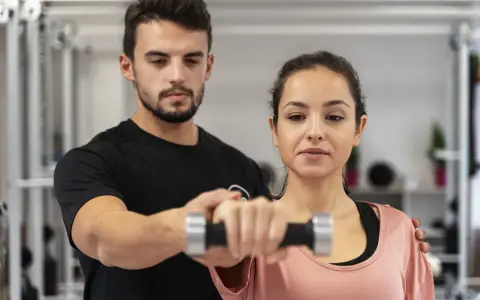 Trening anaerobowy z trenerem. Kobieta ćwiczy z hantlem, mężczyzna koryguje jej ruchy.