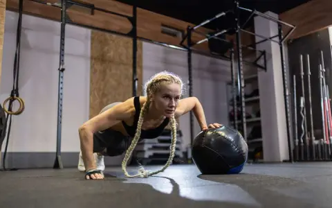 Kobieta wykonuje pompki z piłką lekarską. To przykład treningu, który pokazuje, crossfit co to jest – intensywność i wszechstronność.