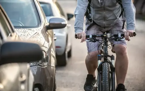 Rowerzysta jedzie obok zaparkowanych samochodów. Warto pamiętać, po jakich drogach nie można jeździć rowerem, by uniknąć niebezpiecznych sytuacji.