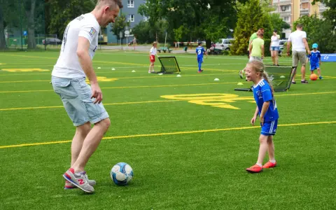 Trening piłki nożnej trwa w najlepsze! Tata uczy córkę dryblingu na zielonej murawie.