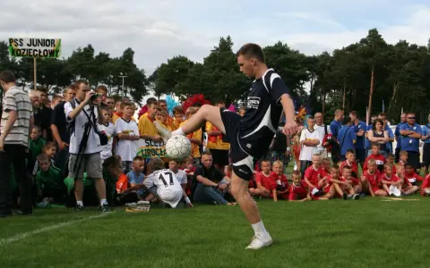 Młody mężczyzna demonstruje żonglerkę piłką na tle tłumu dzieci i dorosłych.
