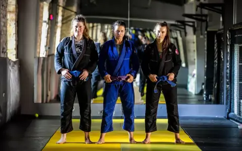 Trzy kobiety w kimonach do BJJ. Środkowa ma purpurowy pas bjj, a pozostałe niebieskie.