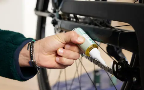 Osoba aplikuje smar na łańcuch rowerowy, dbając o jego płynne działanie. Czyszczenie łańcucha rowerowego to klucz do sprawnej jazdy.