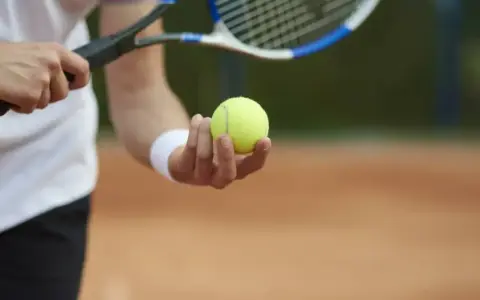 Gracz trzyma piłkę tenisową, gotowy do serwisu. Kluczowy moment decydującego **tenis tie break**.