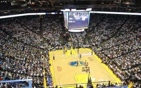 Mecz koszykówki w Oracle Arena. Na boisku gracze, na trybunach tłumy kibiców. Na telebimie widać wynik, który sugeruje, że gra jest w końcowej fazie, być może ostatni z czterech kwart.