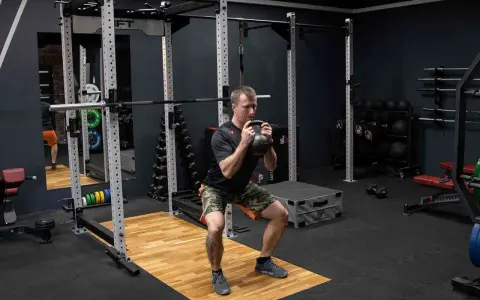 Mężczyzna wykonuje przysiad z kettlebell trzymanym w chwycie nachwyt i podchwyt.
