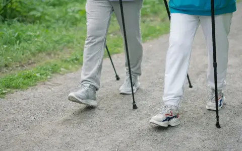 Dwie osoby idące z kijkami po leśnej ścieżce. Pokazują, jak chodzić z kijkami, czerpiąc radość z aktywności na świeżym powietrzu.