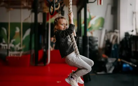 Mała dziewczynka wspina się po linie, ćwicząc siłę i zwinność. To świetna zabawa i aktywność fizyczna, jak aerobik dla dzieci.