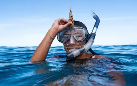 Dziewczyna w masce i fajce do snorkelingu trzyma muszlę na głowie. To właśnie snorkeling!