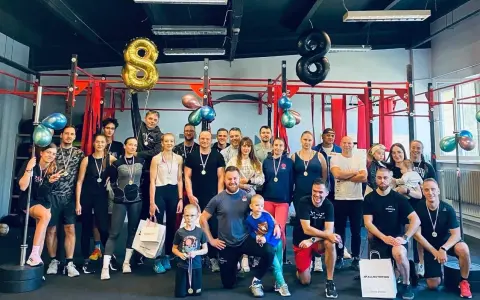 Uśmiechnięta grupa świętuje sukcesy na siłowni. Sportowe grupowe zdjęcie z medalami i balonami w kształcie ósemek.