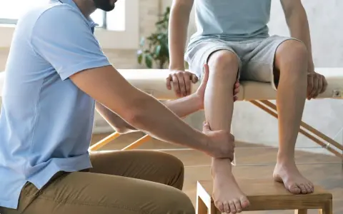 Fizjoterapeuta pomaga w domowej rehabilitacji stawu skokowego, delikatnie masując nogę pacjenta.