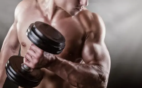 Mężczyzna podnosi ciężarek, jego napięty biceps jest wyraźnie widoczny.