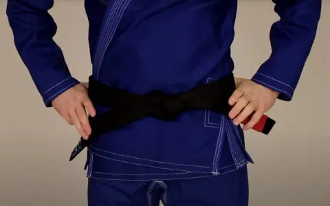 Osoba w niebieskim gi demonstruje wiązanie pasa bjj. Czarny pas jest ciasno zawiązany na wysokości talii.