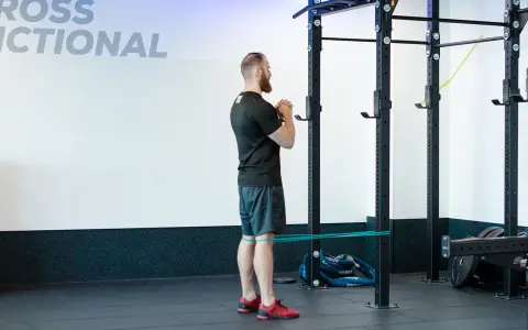 Mężczyzna wykonuje ćwiczenie spanish squat z gumą oporową wokół ud, przygotowując się do przysiadu.