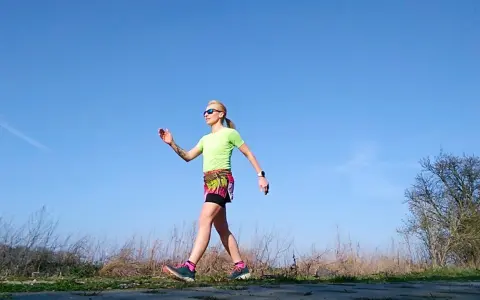 Kobieta w sportowym stroju ćwiczy marsz, stosując metodę Gallowaya. Słoneczny dzień sprzyja aktywności na świeżym powietrzu.
