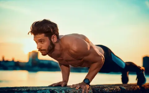Mężczyzna wykonuje pompki na biceps przy wodzie o zachodzie słońca.