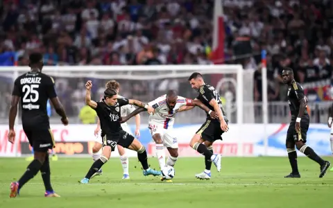 Piłkarze walczą o piłkę, przestrzegając zasad gry. W akcji widać zawodników w białych i czarnych strojach, zmagających się na zielonej murawie stadionu.