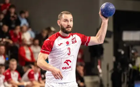 Piłkarz ręczny w białej koszulce z czerwonymi rękawami, z numerem 3, przygotowuje się do rzutu karnego.