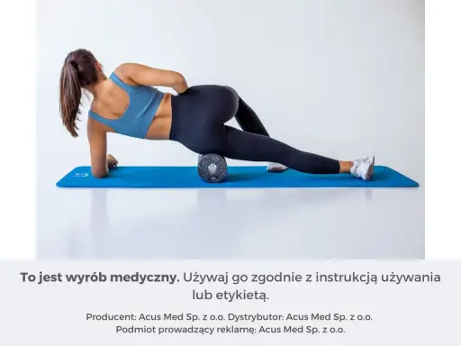 Kobieta na macie rehabilitacyjnej używa wałka do masażu mięśni, aby rozluźnić uda.