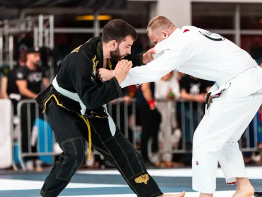 Dwóch zawodników BJJ w kimonach walczy na macie. Jeden w czarnym, drugi w białym.