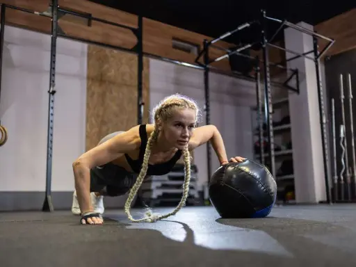 Kobieta wykonuje pompki z piłką lekarską. To przykład treningu, który pokazuje, crossfit co to jest – intensywność i wszechstronność.