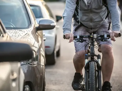 Rowerzysta jedzie obok zaparkowanych samochodów. Warto pamiętać, po jakich drogach nie można jeździć rowerem, by uniknąć niebezpiecznych sytuacji.