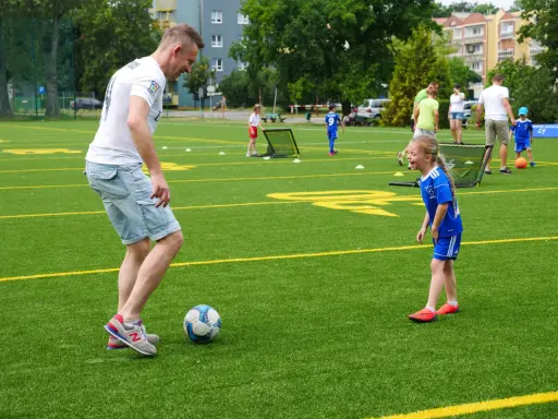 Trening piłki nożnej trwa w najlepsze! Tata uczy córkę dryblingu na zielonej murawie.