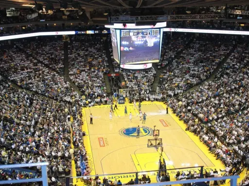 Mecz koszykówki w Oracle Arena. Na boisku gracze, na trybunach tłumy kibiców. Na telebimie widać wynik, który sugeruje, że gra jest w końcowej fazie, być może ostatni z czterech kwart.
