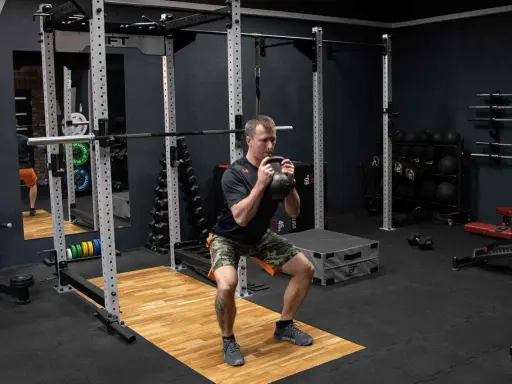 Mężczyzna wykonuje przysiad z kettlebell trzymanym w chwycie nachwyt i podchwyt.