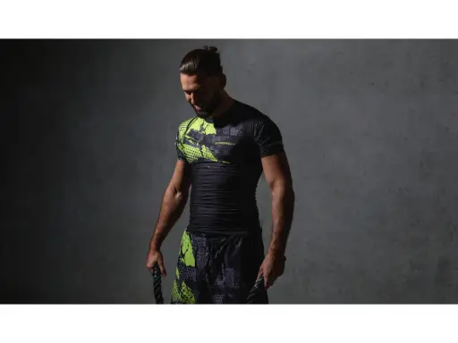 Mężczyzna w czarnym rashguardzie z neonowymi wstawkami i spodenkami, trzymający liny treningowe. Rashguard co to? Odzież sportowa.
