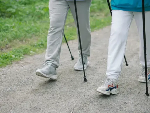 Dwie osoby idące z kijkami po leśnej ścieżce. Pokazują, jak chodzić z kijkami, czerpiąc radość z aktywności na świeżym powietrzu.