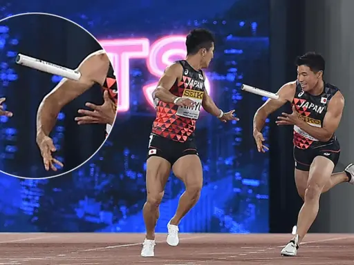 Dwóch lekkoatletów z Japonii w trakcie biegu z pałeczką. Jeden z nich biegnie, drugi wyciąga rękę po pałeczkę.