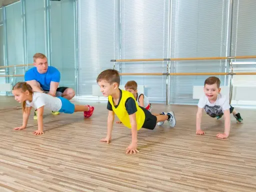 Dzieci wykonują ćwiczenia na brzuch w domu pod okiem trenera.