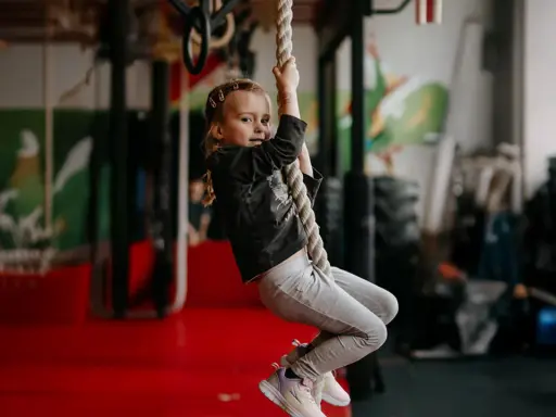 Mała dziewczynka wspina się po linie, ćwicząc siłę i zwinność. To świetna zabawa i aktywność fizyczna, jak aerobik dla dzieci.
