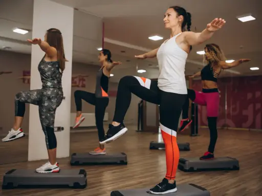 Kobiety wykonują ćwiczenia aerobowe na stepach w sali gimnastycznej.