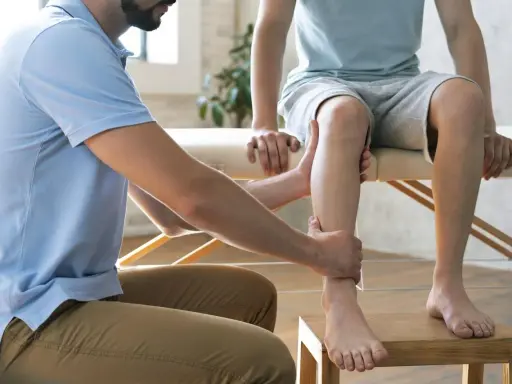 Fizjoterapeuta pomaga w domowej rehabilitacji stawu skokowego, delikatnie masując nogę pacjenta.