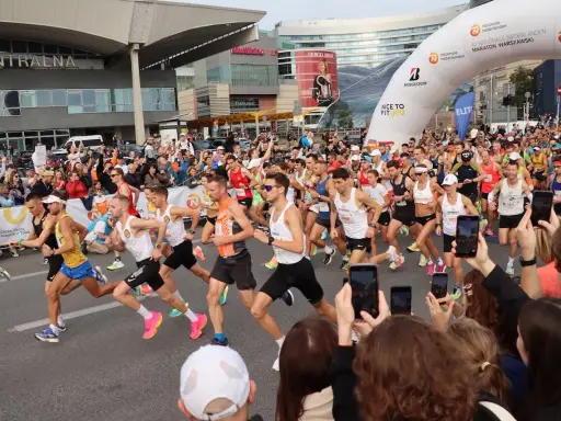 Uczestnicy maratonu w Warszawie, gotowi do startu. To świetny przykład, jak przygotować się do maratonu: trening, determinacja i wsparcie kibiców.