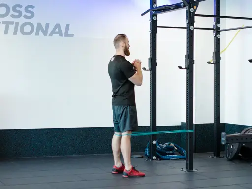Mężczyzna wykonuje ćwiczenie spanish squat z gumą oporową wokół ud, przygotowując się do przysiadu.