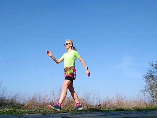 Kobieta w sportowym stroju ćwiczy marsz, stosując metodę Gallowaya. Słoneczny dzień sprzyja aktywności na świeżym powietrzu.