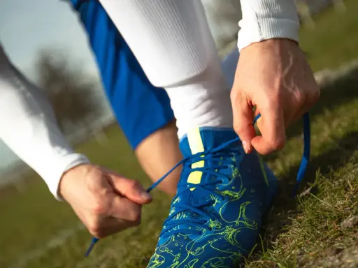 Piłkarz wiąże sznurówki niebieskich butów na zielonej murawie. Ile zmian w piłce nożnej czeka na boisku?