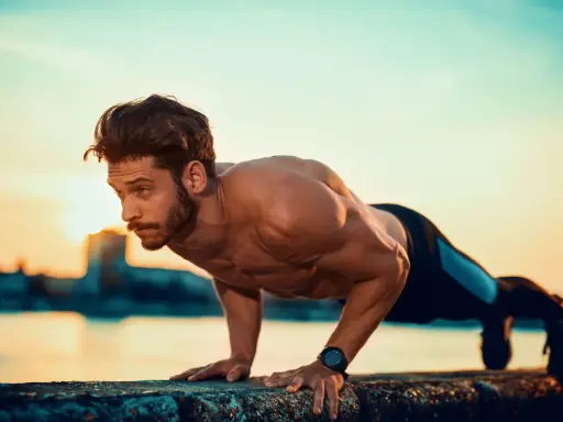 Mężczyzna wykonuje pompki na biceps przy wodzie o zachodzie słońca.