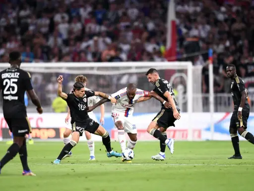 Piłkarze walczą o piłkę, przestrzegając zasad gry. W akcji widać zawodników w białych i czarnych strojach, zmagających się na zielonej murawie stadionu.