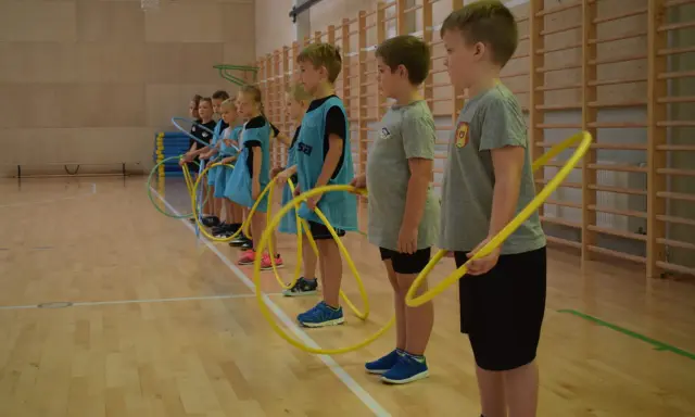 Dzieci z klas 1-3 na lekcji WF ćwiczą z hula-hop. Radosne gry i zabawy sportowe.