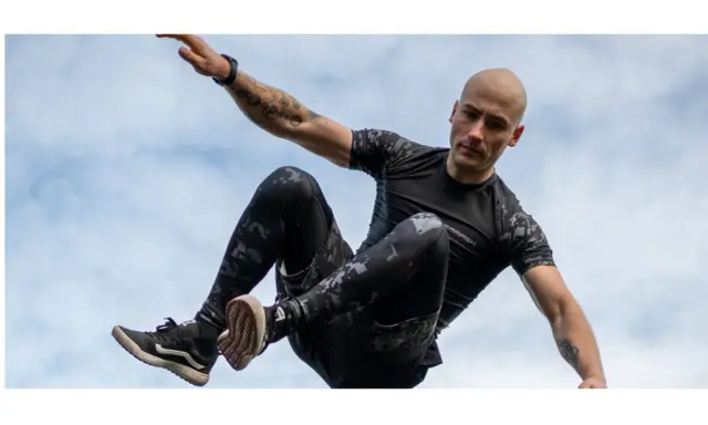 Mężczyzna w ruchu, jakby ćwiczył hiit. Co to za trening? Dynamiczne skoki i akrobacje na tle nieba.