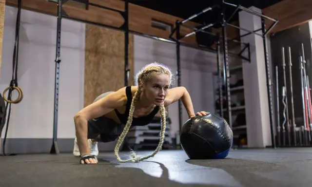 Kobieta wykonuje pompki z piłką lekarską. To przykład treningu, który pokazuje, crossfit co to jest – intensywność i wszechstronność.