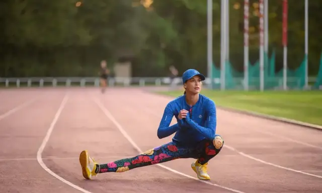 Królowa sportu w kwiecistych legginsach rozciąga się na bieżni.