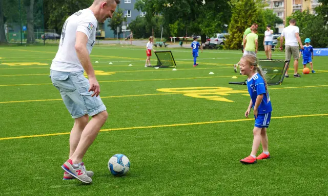 Trening piłki nożnej trwa w najlepsze! Tata uczy córkę dryblingu na zielonej murawie.